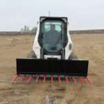 Front-facing view of a skid steer loader with Messer Attachments 84-inch manure fork and bright red tines