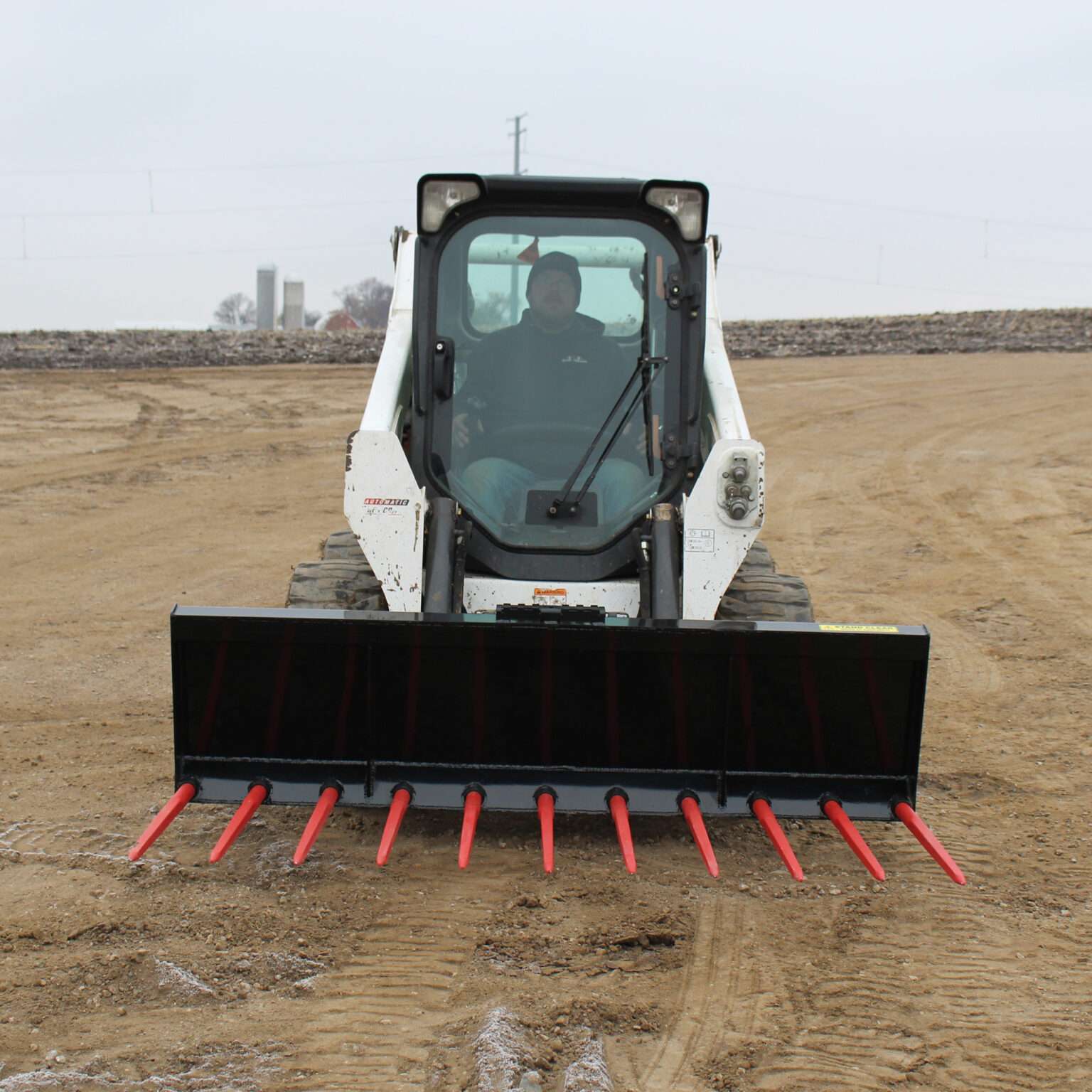 Front-facing view of a skid steer loader with Messer Attachments 84-inch manure fork and bright red tines