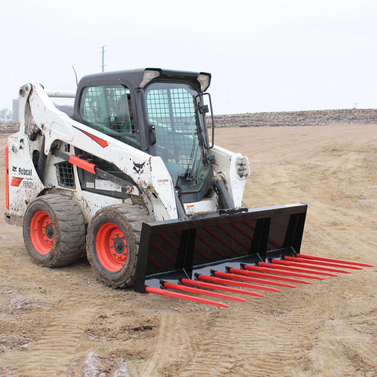 Angled side view of a skid steer loader showcasing Messer Attachments heavy-duty manure fork with spring steel tines