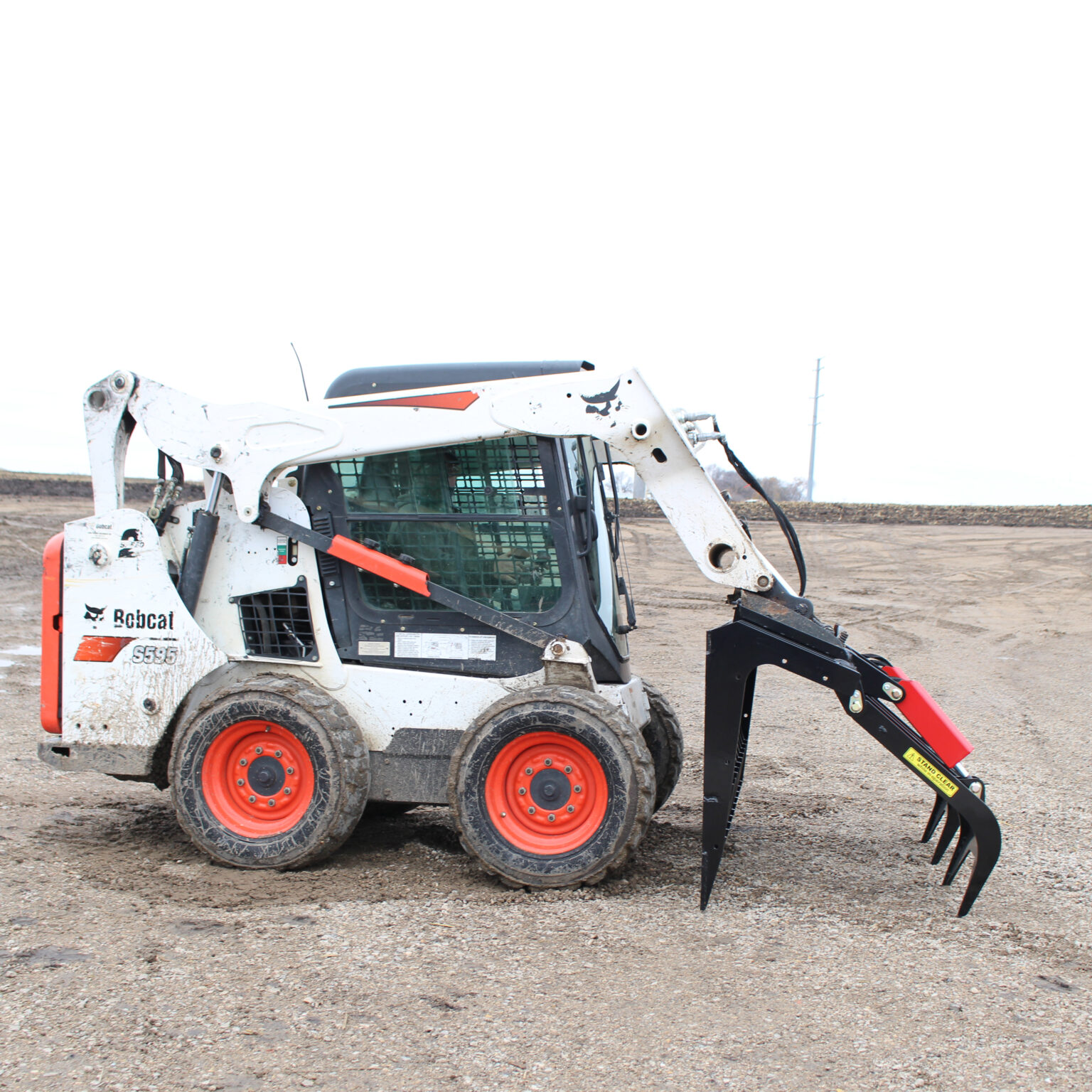 A Bobcat skid-steer loader with a Messer brush attachment featuring an open grapple on the ground.